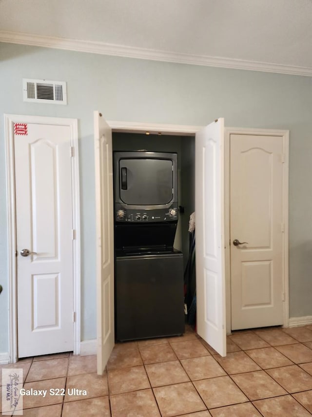 laundry room featuring light tile patterned flooring, stacked washing maching and dryer, and crown molding