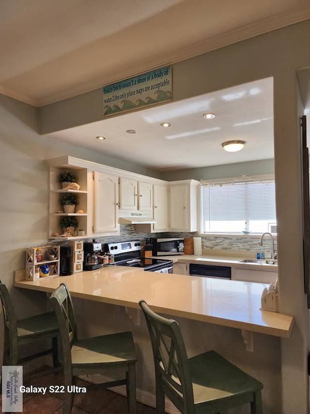 kitchen featuring a kitchen bar, decorative backsplash, stainless steel appliances, sink, and white cabinetry