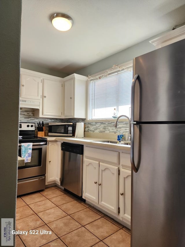 kitchen featuring decorative backsplash, stainless steel appliances, extractor fan, white cabinets, and light tile patterned flooring