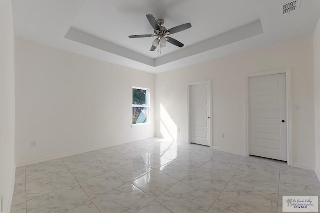 spare room with ceiling fan and a tray ceiling