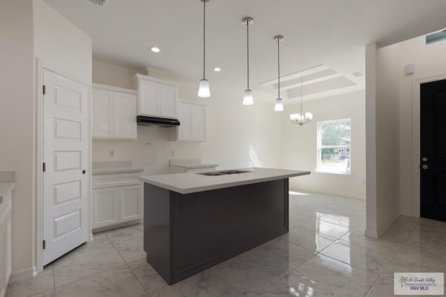 kitchen with white cabinets, a center island with sink, hanging light fixtures, and a chandelier