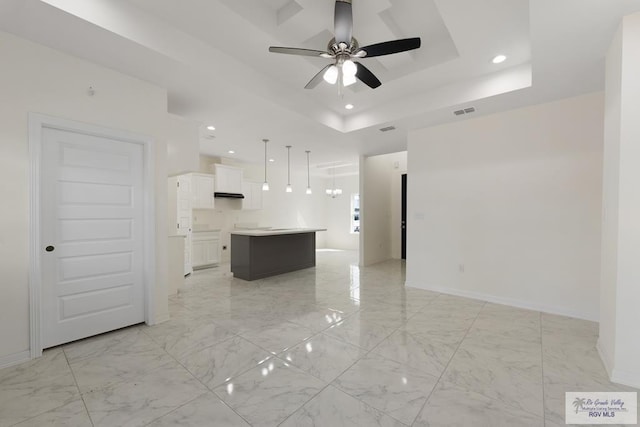 kitchen with white cabinetry, ceiling fan, hanging light fixtures, a raised ceiling, and a kitchen island