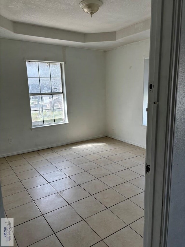 tiled spare room with a tray ceiling and a textured ceiling