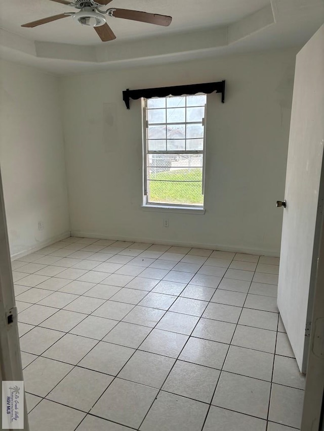 empty room with a raised ceiling, ceiling fan, and light tile patterned floors