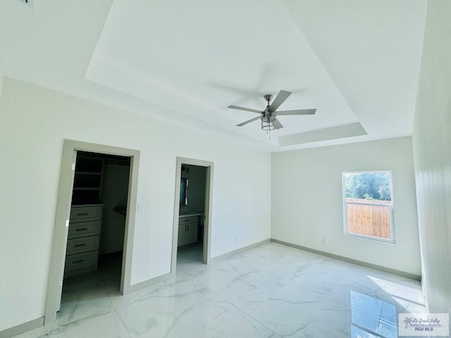 unfurnished bedroom with ensuite bath, ceiling fan, a tray ceiling, a walk in closet, and a closet