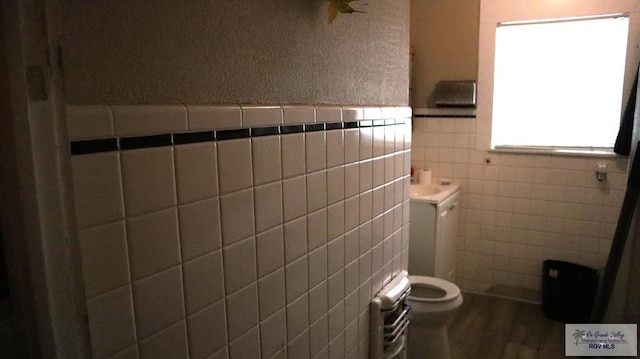 bathroom featuring radiator heating unit, toilet, tile walls, and wood-type flooring