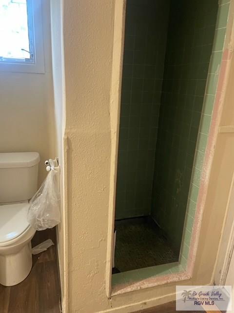 bathroom featuring wood-type flooring, a tile shower, and toilet