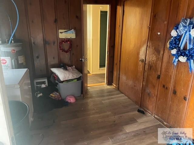 hallway with electric water heater, wooden walls, and light hardwood / wood-style flooring