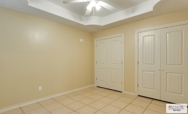 unfurnished bedroom with a tray ceiling, ceiling fan, and light tile patterned flooring