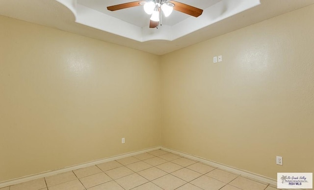 tiled empty room with a raised ceiling and ceiling fan