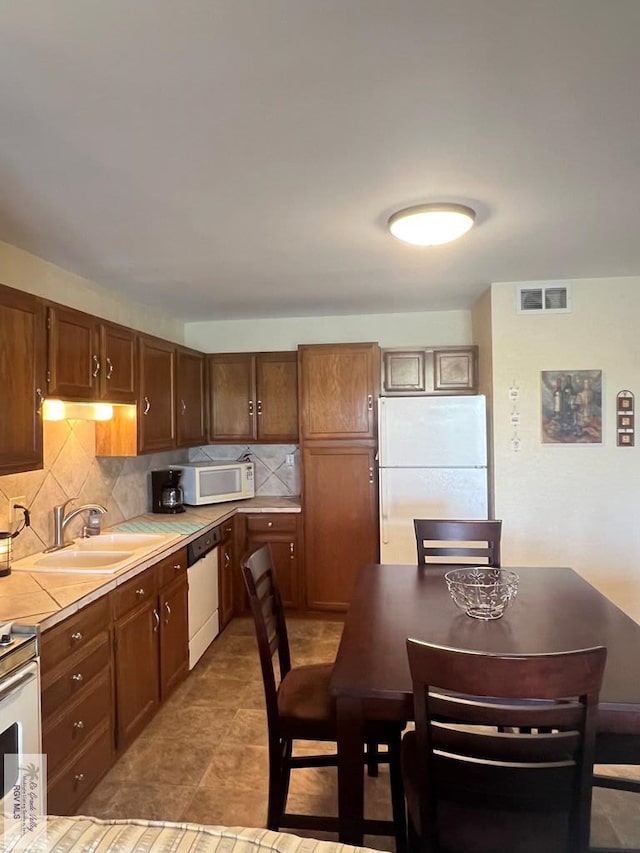 kitchen featuring visible vents, tile counters, white appliances, a sink, and backsplash