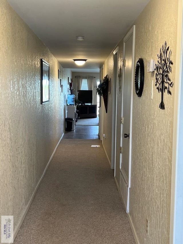 hall with carpet flooring, baseboards, and a textured wall