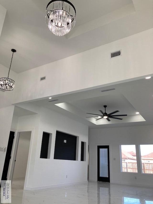 interior space with ceiling fan with notable chandelier and a raised ceiling