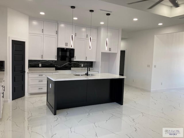 kitchen featuring a kitchen island with sink, white cabinets, sink, hanging light fixtures, and light stone counters