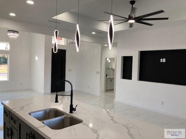 kitchen with decorative light fixtures, light stone countertops, sink, and ceiling fan with notable chandelier