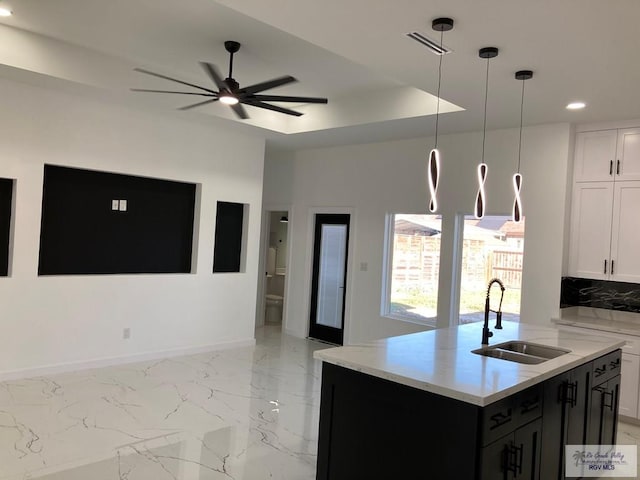 kitchen featuring ceiling fan, a kitchen island with sink, sink, white cabinetry, and hanging light fixtures