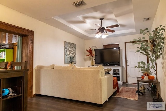 living room with dark hardwood / wood-style flooring, a raised ceiling, and ceiling fan