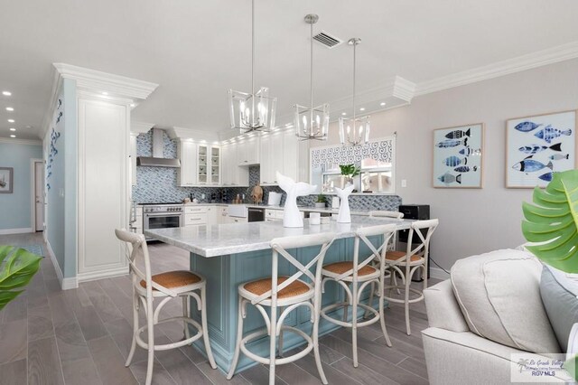 kitchen featuring hanging light fixtures, wall chimney exhaust hood, a kitchen island, a kitchen bar, and white cabinetry