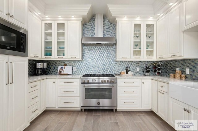 kitchen featuring backsplash, light stone counters, wall chimney range hood, and stainless steel appliances