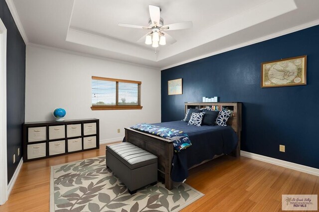 bedroom featuring a raised ceiling, ceiling fan, crown molding, and light wood-type flooring