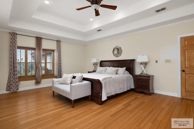 bedroom with ceiling fan, light wood-type flooring, and a tray ceiling