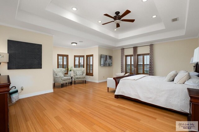 bedroom featuring a tray ceiling, multiple windows, ceiling fan, and light hardwood / wood-style flooring