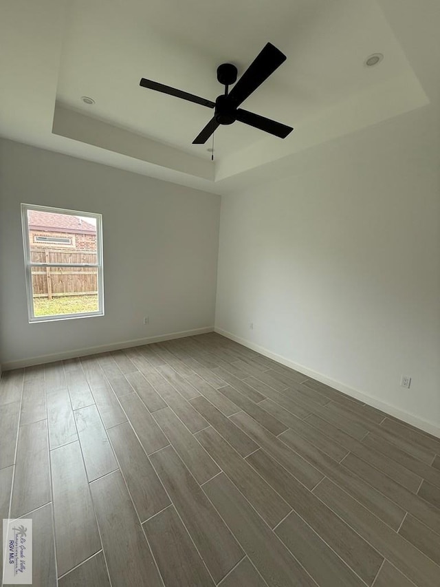 empty room with a raised ceiling, baseboards, a ceiling fan, and dark wood finished floors