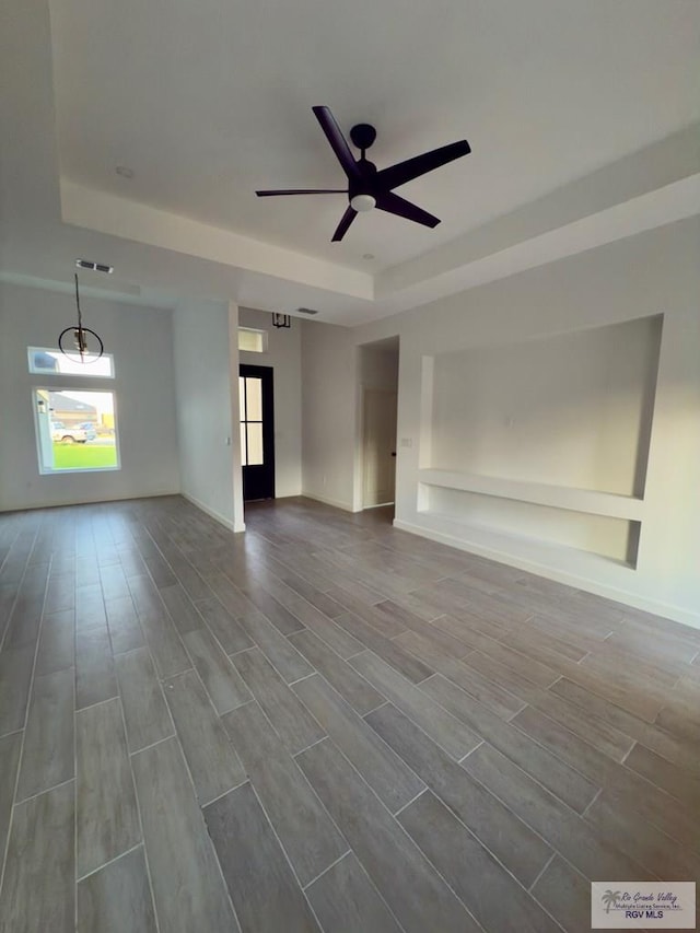 unfurnished living room with a tray ceiling, dark wood-type flooring, and a ceiling fan