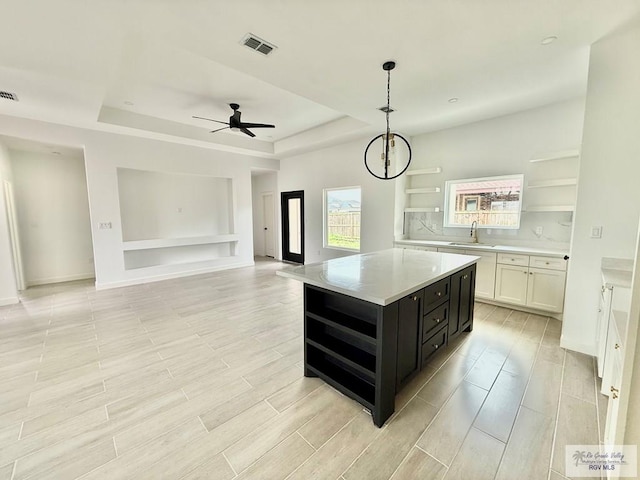kitchen with a tray ceiling, dark cabinets, visible vents, open shelves, and light countertops