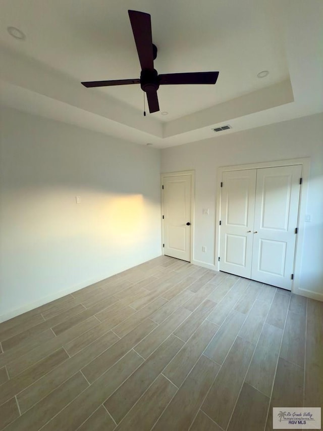 unfurnished bedroom with baseboards, a raised ceiling, visible vents, and wood finished floors