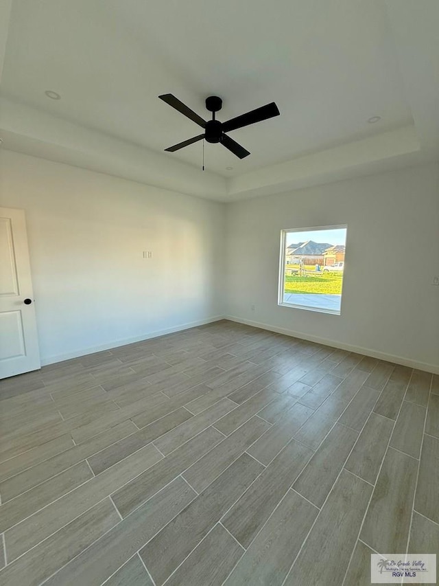 spare room featuring baseboards, wood finished floors, a raised ceiling, and ceiling fan