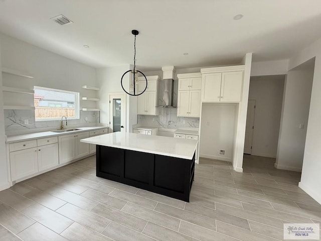 kitchen with a sink, open shelves, visible vents, wall chimney exhaust hood, and a kitchen island