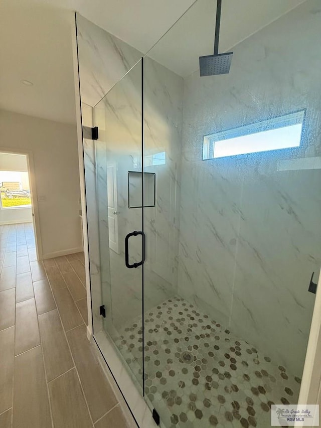full bath with a marble finish shower, baseboards, and a healthy amount of sunlight
