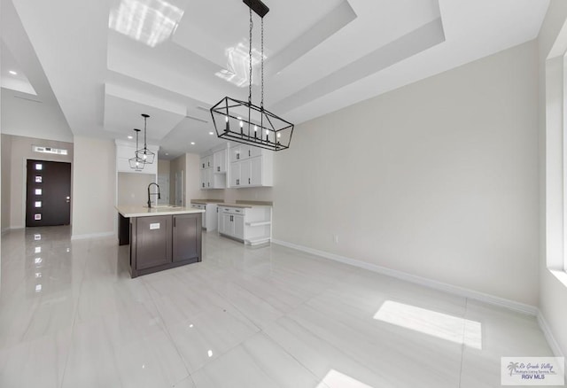 kitchen featuring a sink, white cabinetry, baseboards, open floor plan, and a tray ceiling