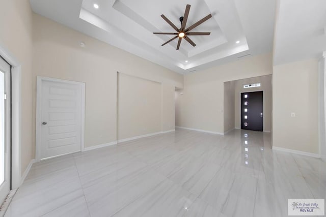 interior space with a raised ceiling, ceiling fan, a towering ceiling, and baseboards