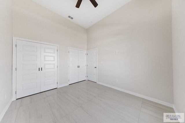 unfurnished bedroom featuring high vaulted ceiling, visible vents, baseboards, and two closets