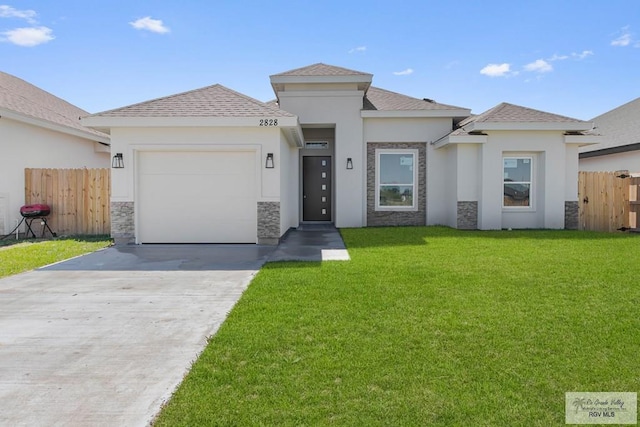 prairie-style home featuring a front lawn, stone siding, fence, and an attached garage