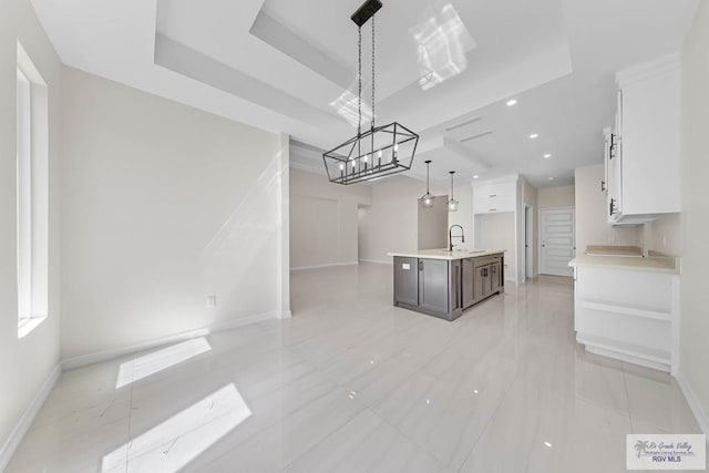 kitchen with a sink, white cabinetry, light countertops, a tray ceiling, and an island with sink