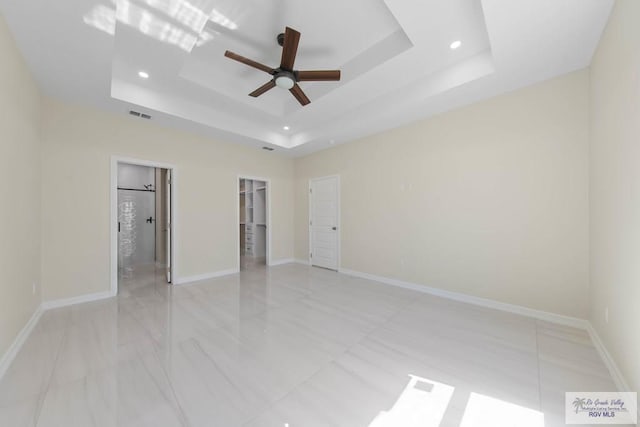 unfurnished bedroom with a raised ceiling, visible vents, a spacious closet, and baseboards