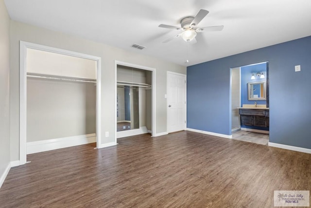 unfurnished bedroom featuring multiple closets, wood finished floors, and baseboards
