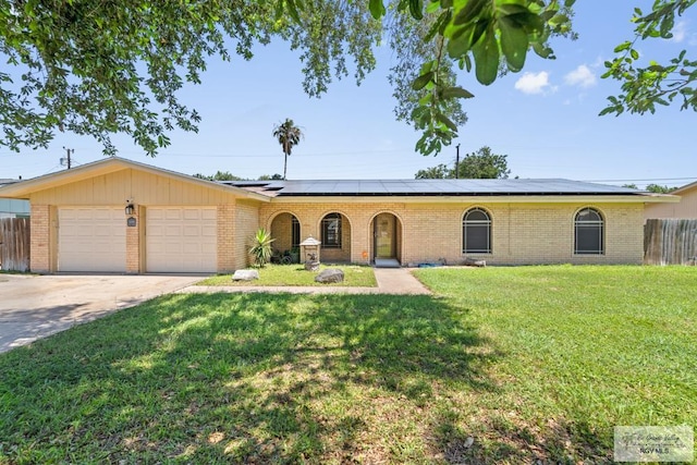 ranch-style house with brick siding, an attached garage, roof mounted solar panels, and concrete driveway