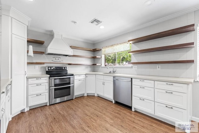 kitchen with open shelves, stainless steel appliances, premium range hood, light countertops, and a sink
