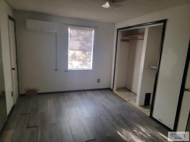 unfurnished bedroom with dark hardwood / wood-style floors, an AC wall unit, and a closet