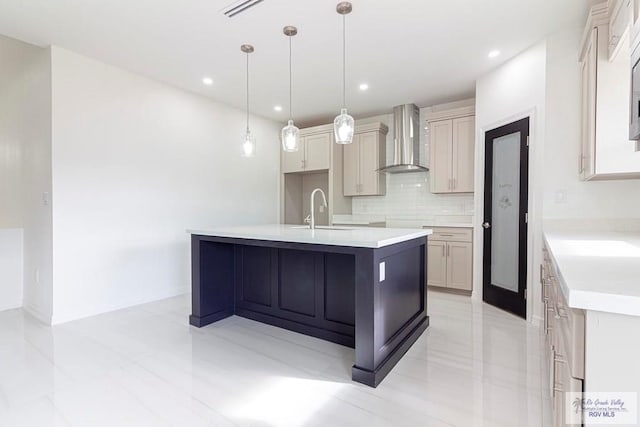 kitchen with decorative backsplash, wall chimney exhaust hood, a kitchen island with sink, sink, and pendant lighting