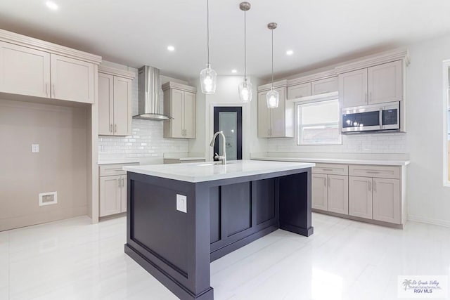 kitchen featuring decorative light fixtures, gray cabinets, a kitchen island with sink, and wall chimney exhaust hood