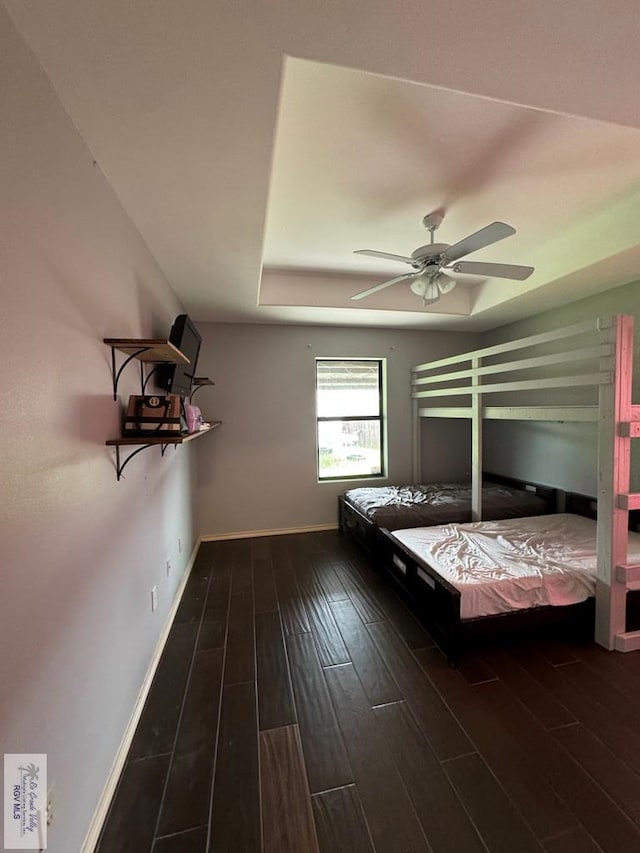 unfurnished bedroom with ceiling fan, dark hardwood / wood-style floors, and a raised ceiling