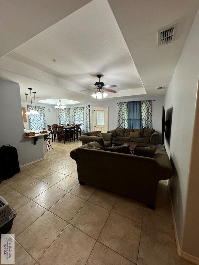 tiled living room with a tray ceiling and ceiling fan