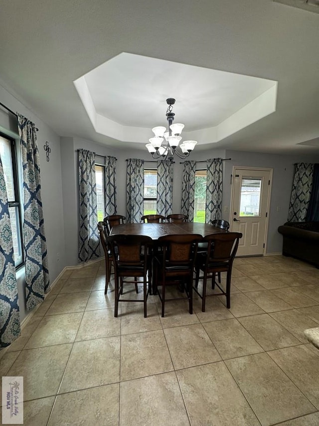 tiled dining space featuring a raised ceiling, plenty of natural light, and a chandelier