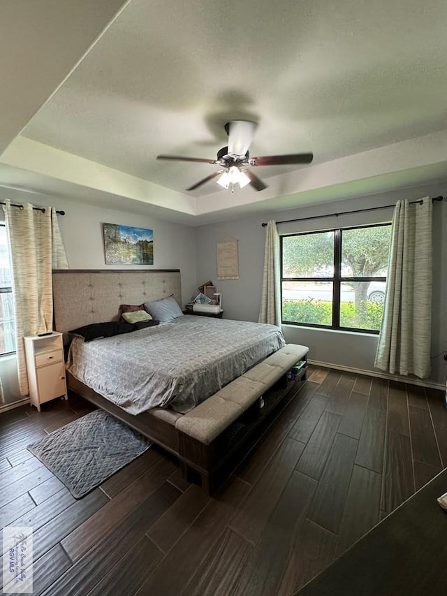 bedroom with a tray ceiling, ceiling fan, and dark wood-type flooring