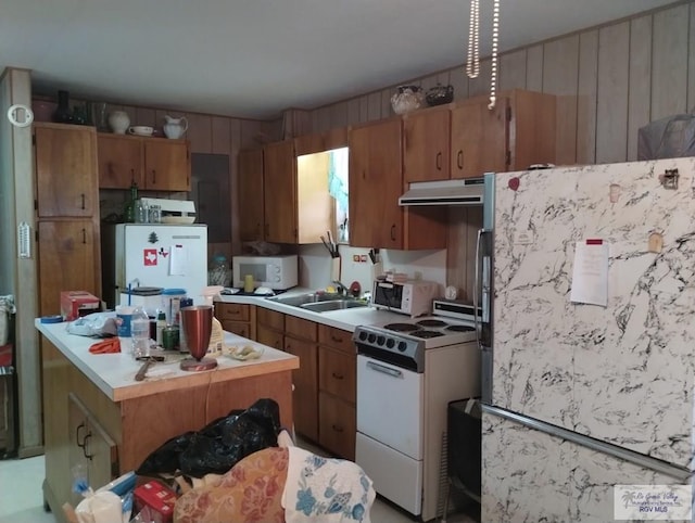 335 Edwards St, San Benito, TX 78586 - kitchen featuring white appliances, under cabinet range hood, light countertops, brown cabinetry, and wood walls